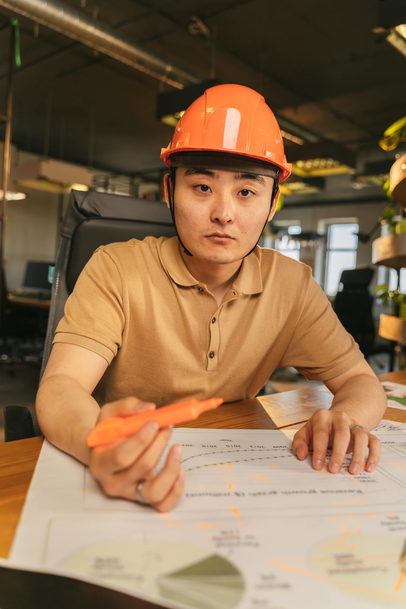 Young male architect with helmet reviewing blueprints in a modern office setting.